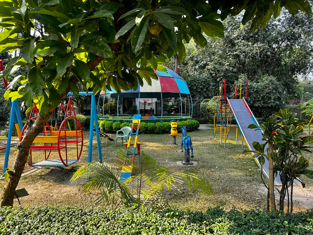 A vibrant outdoor children’s playground at Barnochata, featuring colorful swings, slides, and spring riders surrounded by green foliage in a peaceful garden setting.