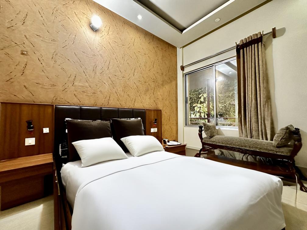 A cozy bedroom in Dhaka hotel with a comfortable bed, dresser, and a ceiling fan. Perfect for a relaxing stay in Savar or Barnochata.