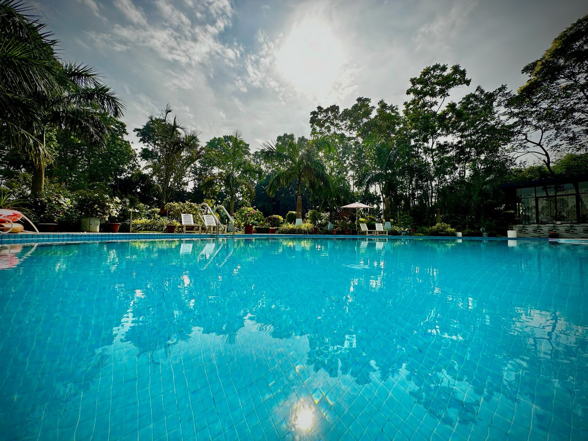 Serene pool at Barnochata Resort in Savar near Dhaka, with crystal clear blue waters, surrounded by lush tropical foliage under a bright sky