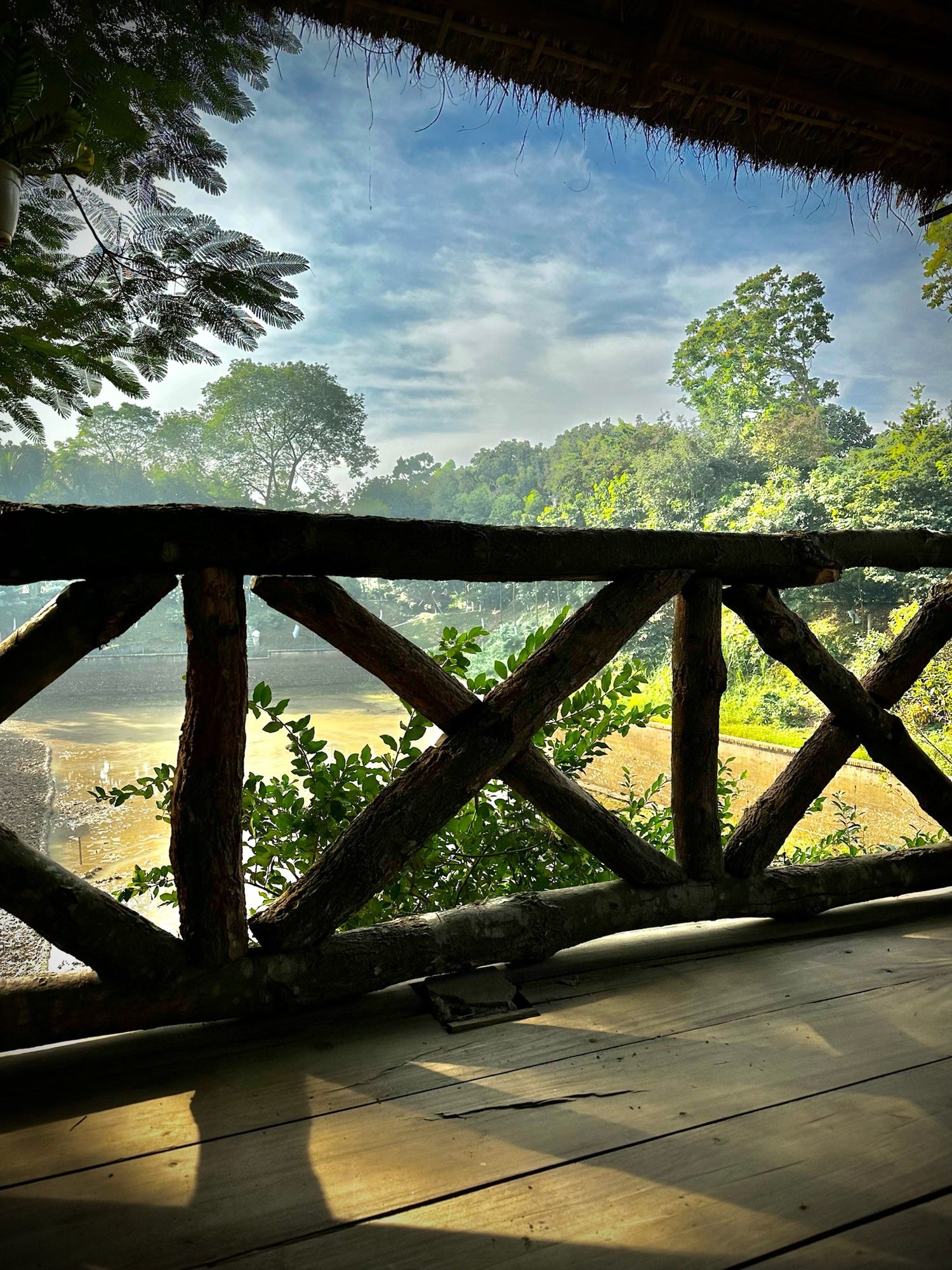 View from a rustic gazebo at Barnochata, a Dhaka hotel and resort in Savar, overlooking the serene natural landscape and water.