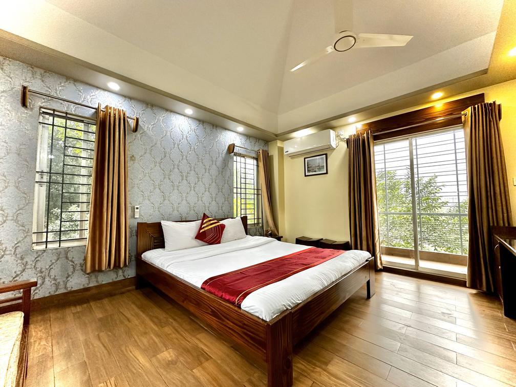 A cozy bedroom in Dhaka hotel with a comfortable bed, a ceiling fan, and a wooden floor.
