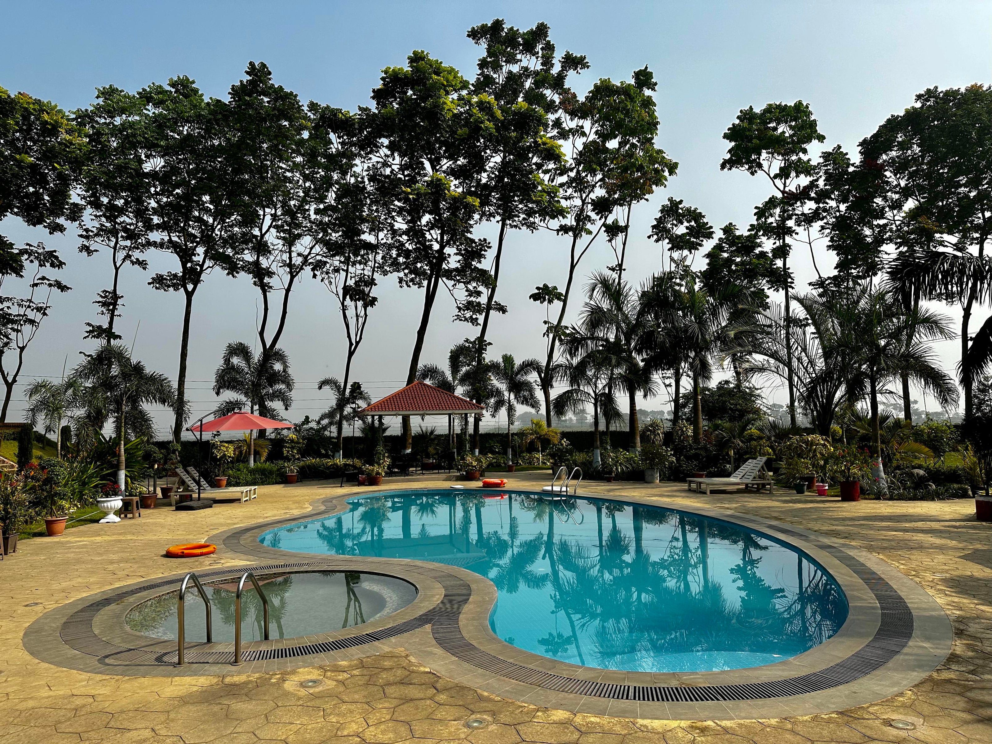 Scenic outdoor swimming pool at Barnochata, a premium Dhaka hotel and resort in Savar, framed by tall trees and clear skies.