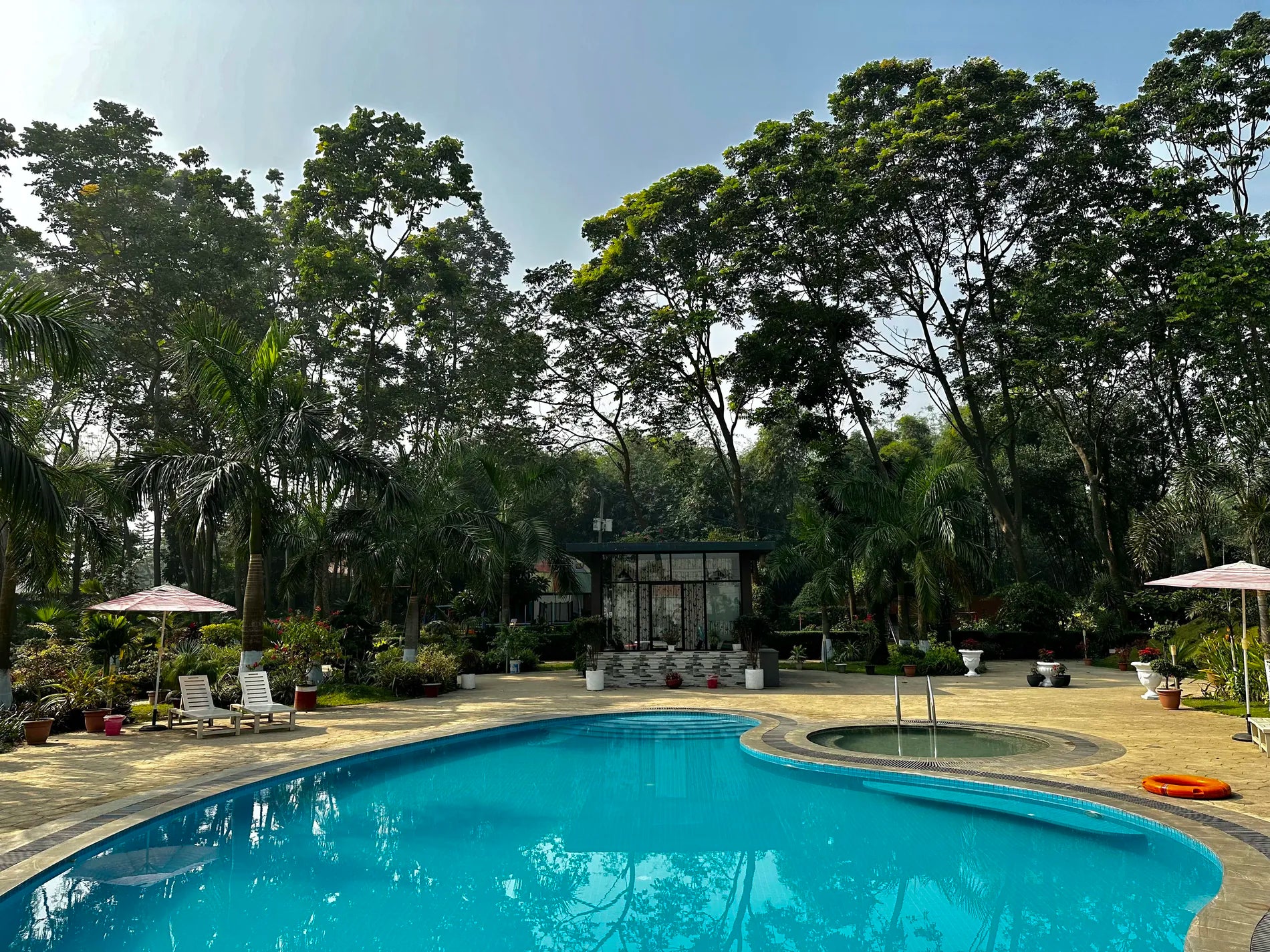 A serene outdoor resort pool framed by tall tropical trees at a property near Dhaka, Bangladesh